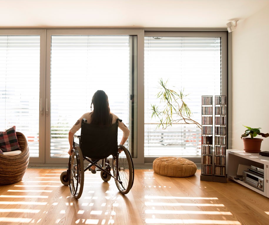 Femme dans un fauteuil roulant devant une porte-fenêtre avec volets roulants