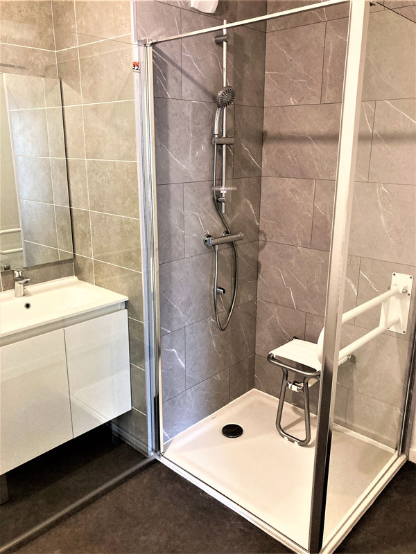 Agrandissement de l’espace douche pour couple PMR. (Intégration siège + barre appui + paroi avec porte grande ouverture)