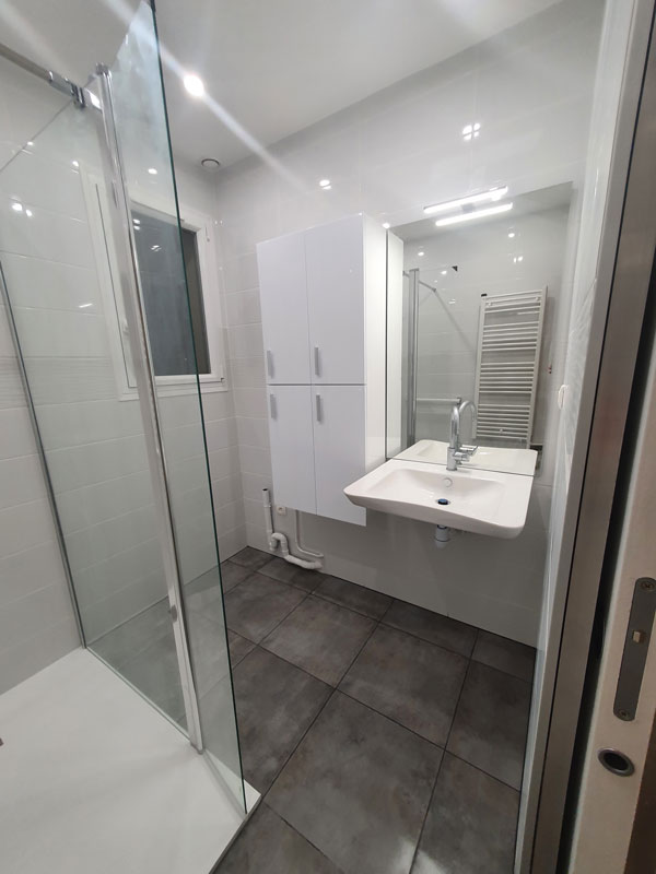 Salle de bain complète avec douche de plain-pied, vasque suspendue, rangement, faïence aux murs et carrelage antidérapant au sol, pose d’une porte à galandage